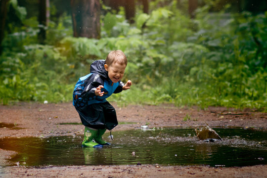A little boy is jumping in a muddy puddle. Image with selective focus