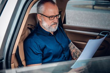 Fototapeta Shot of cool old man businessperson with documents on road trip inside of car. obraz