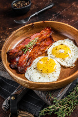 Traditional English breakfast with fried eggs and bacon in wooden plate. Dark background. Top view