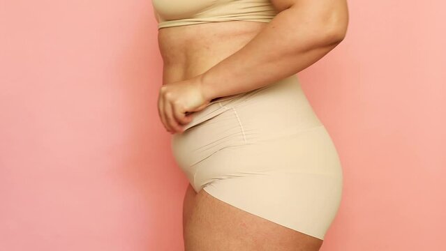 Cropped studio shot of fat overweight woman in special fitness beige shape wear. Fast gain weight with pregnancy. Body health care. Visceral obesity, folds flabs of dehydrated dozed body. Side view