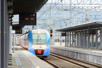 Arrival of a blue suburban electric train at a passenger station. Empty platform in front of the railway track.
