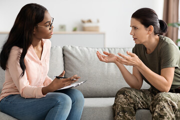 Worried female soldier talking to black psychologist during therapy session at office