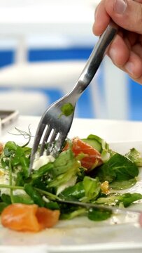 Caucasian ethnicity human hands holding fork and knife, cut herbs in tasty fresh salad.