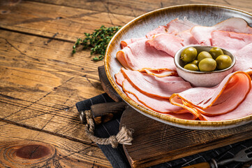 Smoked Ham slices in plate with olives. Wooden background. Top view. Copy space