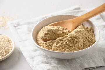 Sesame flour in white bowl for cooking gluten-free dessert. Good source of protein, minerals, natural antioxidants and vitamins. Close up.