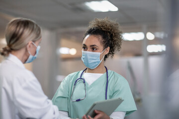 Two female medical practitioners discussing patient treatment wearing face masks