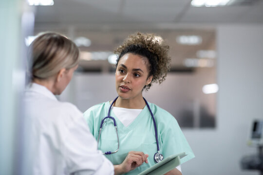 Two female medical practitioners discussing patient treatment using a digital tablet