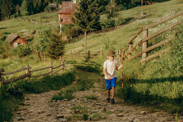 A boy walks along a dirt road in a village in the summer in the Alpine mountains.