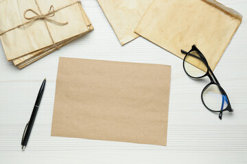 Old letters, blank card, pen and glasses on white wooden table, flat lay