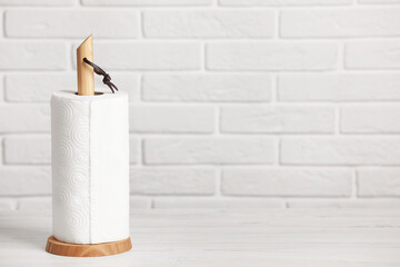 Holder with roll of paper towels on white wooden table near brick wall. Space for text