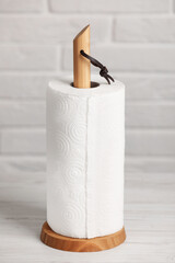 Holder with roll of paper towels on white wooden table near brick wall