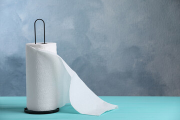 Holder with roll of white paper towels on turquoise wooden table. Space for text