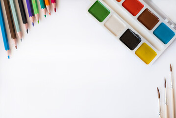 Pencils, watercolors and brushes lie on a white paper background with space for writing text.