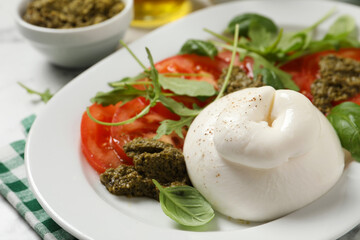 Delicious burrata salad with tomatoes, arugula and pesto sauce on table, closeup