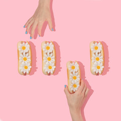 Spring creative layout with hands taking white flowers in hot dog buns pastel pink background. 80s or 90s retro fashion aesthetic bloom concept. Minimal romantic food idea.