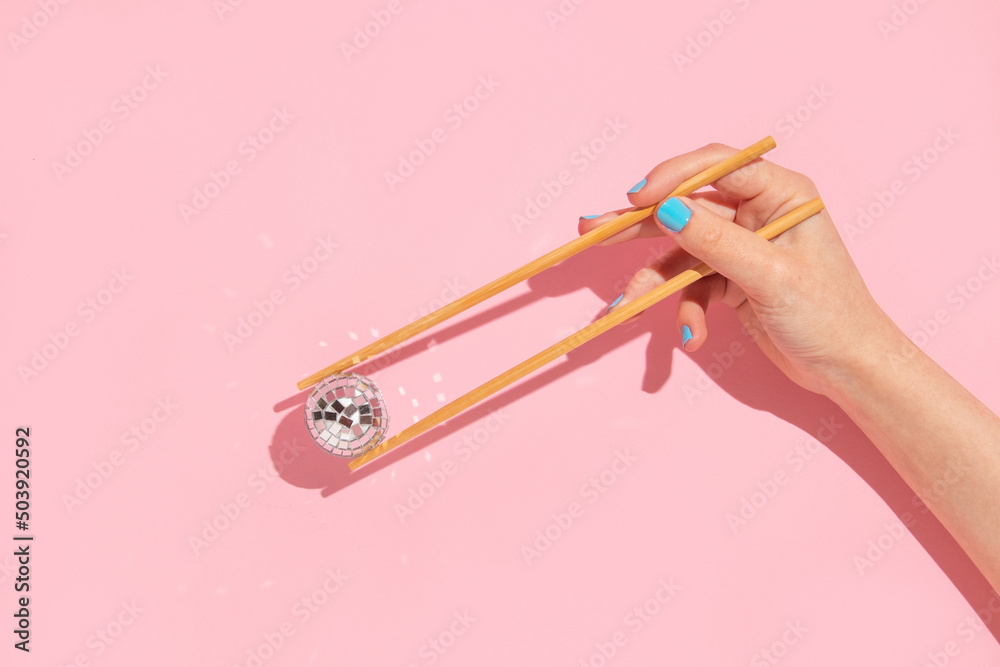 Sticker creative layout with woman hand holding chopsticks and disco ball decoration on pastel pink backgrou