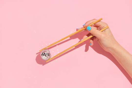 Creative layout with woman hand holding chopsticks and disco ball decoration on pastel pink background. 80s or 90s retro fashion aesthetic party concept. Minimal romantic food idea.