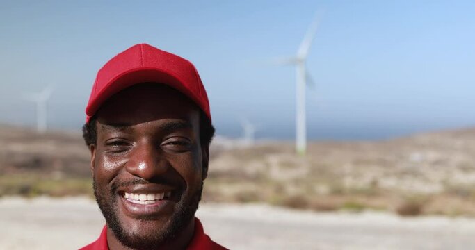 African engineer worker smiling on camera with windmill farm in background