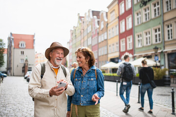 Portrait of happy senior couple tourists using smartphone outdoors in historic town - obrazy, fototapety, plakaty