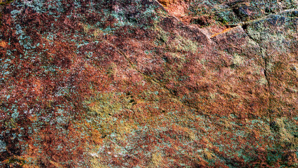 Pattern of granite stone wall covered with moss and lichen, as a background, closeup, details.