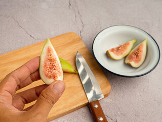 Hand holding of a half fig fruit with figs on a white dish background