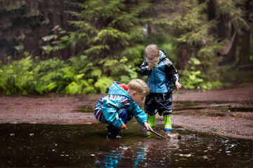 Two little boys are playing in a muddle puddle. There is a reflection in a puddle. Image with...