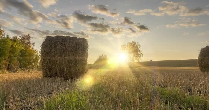 4K UHD flat hill meadow timelapse at the summer sunset time. Wild nature and rural haystacks on grass field. Sun rays and green trees. Motorised dolly slider