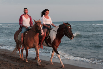 a loving young couple in summer clothes riding a horse on a sandy beach at sunset. Sea and sunset in the background. Selective focus 