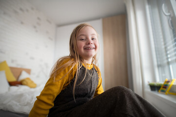 Happy little girl with Down syndrome sitting on bed at home.