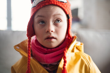 Little girl with Down syndrome looking at camera outoors in winter against brick wall.