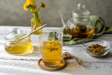 Dandelion tea and honey on the white wooden table with tea pot, dandelion flowers, dry mix for tea