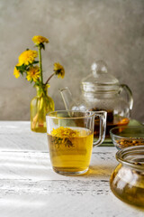 Healthy herbal tea from dandelions on the white wooden table with tea pot, dandelion flowers, honey
