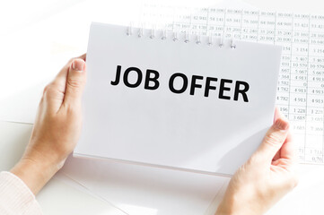 JOB OFFER text on a notebook in the hands of a girl sitting at a table