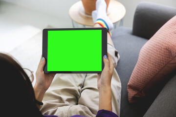 Over shoulder Girl using tablet computer on sofa in living room with blank green screen, Work from home concept.