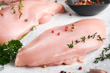 Chicken breast. Raw chicken breast fillets on black ceramic plate on wooden cutting board with herbs and spices on old grey table background. Top view with copy space.