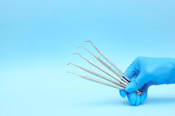 A hand in a blue glove holds dental instruments. Close-up on a blue background. Place to copy. Medicine, dentistry