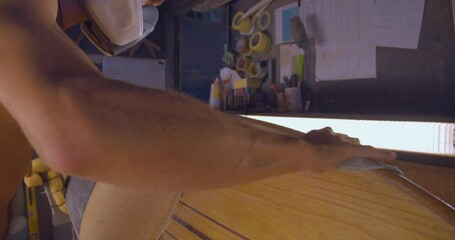Surfboard Maker Sanding Side Of A Wooden Surfboard With Sandpaper At Workshop. medium shot - Powered by Adobe