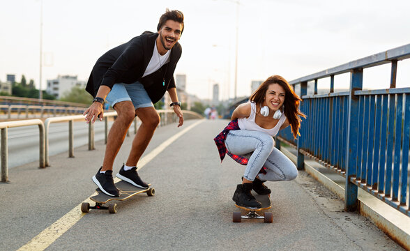 Portrait of happy couple having fun while driving a long board in city. People skateboard concept