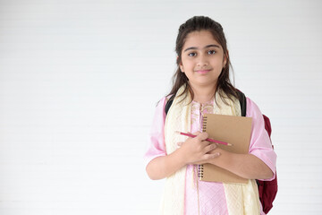 cute Indian girl smiling and writing on notebook for learning, education concept