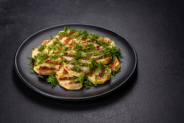 Delicious grilled potato slices with spices and herbs on a black plate