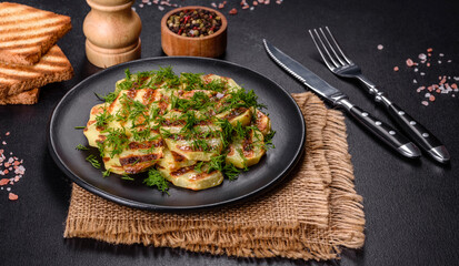Delicious grilled potato slices with spices and herbs on a black plate