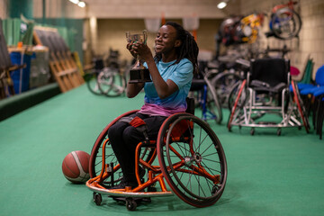 Teenage girl in wheelchair holding basketball trophy