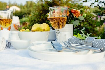 Summer holiday table set up. Elegant table setting with white dishes on a white linen tablecloth. Ripe fruits, drinks in crystal glasses. Table set for outdoor eating in the garden. Soft focus