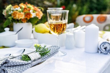 Summer holiday table set up. Elegant table setting with white dishes on a white linen tablecloth. Ripe fruits, drinks in crystal glasses. Table set for outdoor eating in the garden. Soft focus