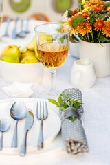 Elegant table setting with white dishes on a white linen tablecloth. Fruits, drinks in crystal glasses. Summer holiday table set up. Outdoor eating on a table in the garden. Vertical shot