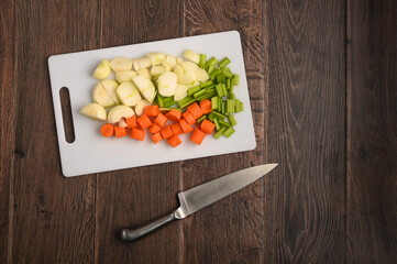 Chopped carrots, onion and celery on a chopping board with a dark wood background