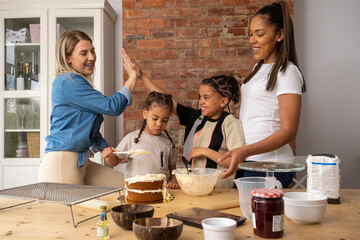 Mothers and sons making cake in kitchen - obrazy, fototapety, plakaty