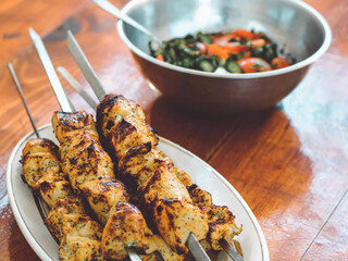 Shish kebab and a plate with chopped vegetables on a wooden surface. Grilled meat.