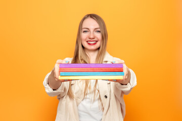 Happy funny caucasian student girl holding a lot of books in her hands isolated over orange studio background. Education concept