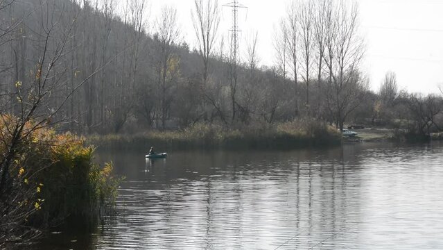 Unidentified man fishing from an inflatable boat on the river in the evening